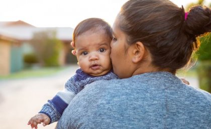 An Indigenous woman kisses a baby looking over her shoulder.